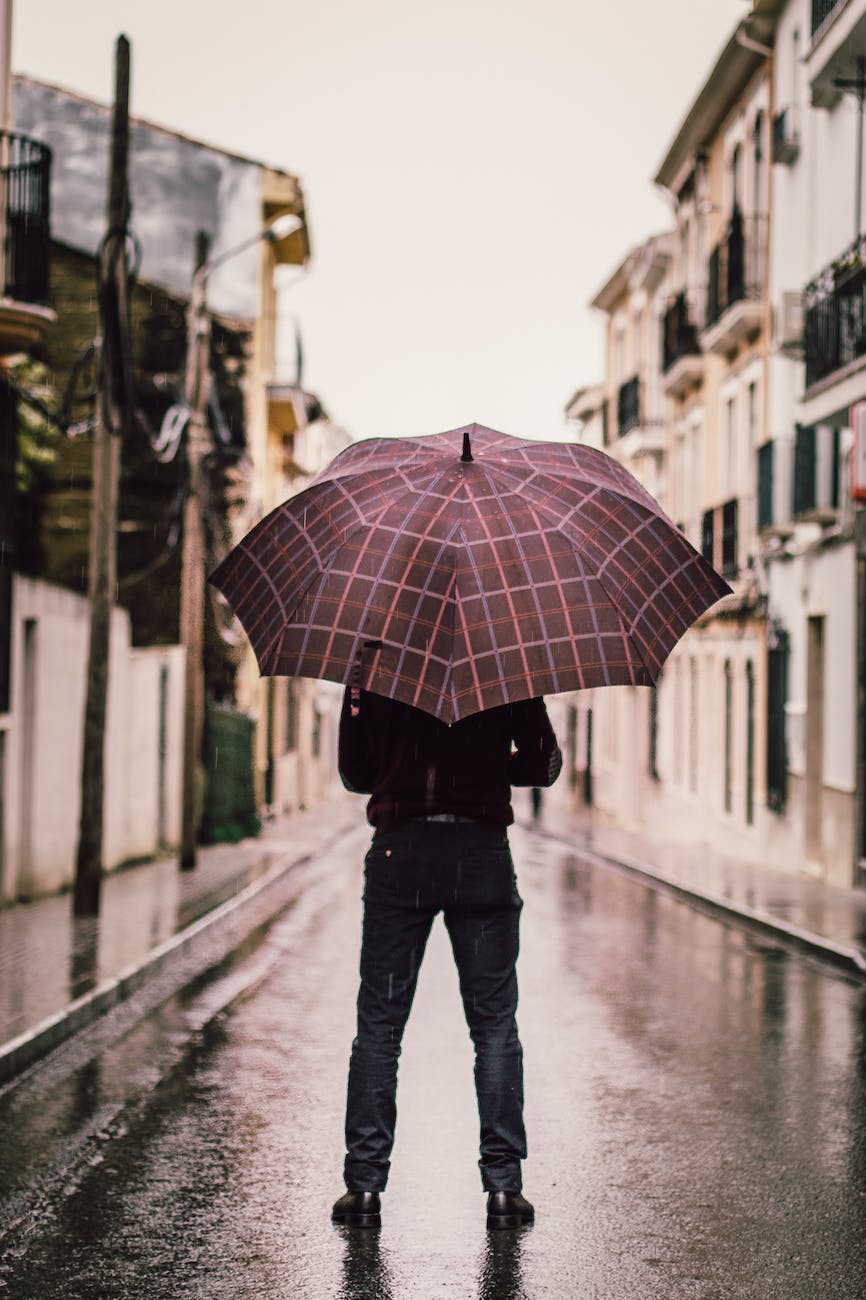 person wearing black pants holding umbrella standing on road